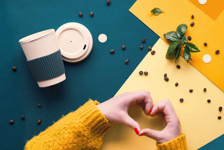 Zero waste coffee concept. Eco friendly reusable coffee cups in hands. Geometric flat lay on split paper. Creative background in dark cyan, orange and yellow colors.の写真素材