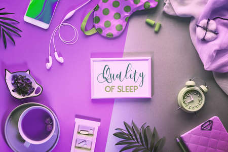 Healthy night sleep creative concept. Sleeping mask, alarm clock, earphones, earplugs, tea and pills. Split neon two tone purple green background with palm leaves. Text "Quality of sleep" in frame.の写真素材