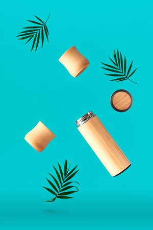 Zero waste tea in insulated bamboo and metal travel flask Travel with homemade tea or herbal infusion in eco friendly insulated bamboo flask. Zero waste concept levitation on cyan background.の写真素材
