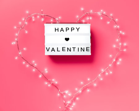 Valentine flat lay, top view on pink background. Lightbox with text Happy Valentine. Light garland...