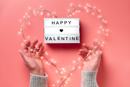 Valentine flat lay, top view on pink background. Lightbox with text Happy Valentine. Light garland...