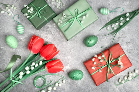 Easter flowers, eggs and gift boxes, flat lay on textured grey background. Red tulips, white baby...