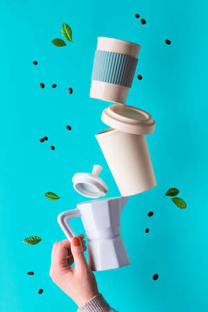 Balancing zero waste coffee pyramid in female hands on blue mint background. Ceramic espresso coffee maker and eco friendly reusable bamboo coffee mugs with silicone. Coffee beans and leaves around.の写真素材