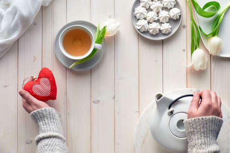 Spring celebration flat lay. Female hands with tea, sweets and tulips on white wooden table. Mothers day, Valentine, international women day 8 or March, birthday or special occasionの写真素材