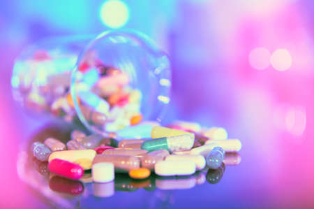 Assorted pills or capsules with medications on dark abstract background with reflection. Bold vibrant colors, futuristic purple, blue and turquoise lights. Shallow DOF, focus on front capsules.の写真素材