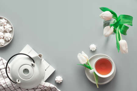 Geometric panoramic flat lay with hands. Cup of black tea, tea pot, sweets and white tulips on grey with copy-space.の写真素材
