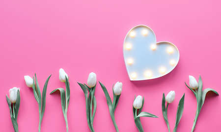 St Valentine's day pink background. Wave parallel geometric line of white tulip flowers. Lightboard in heart shape with illuminated lights. Flat lay, top view, minimal trendy Valentine design concept.の写真素材