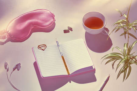 Healthy night sleep creative concept in pink and green. Sleep mask, earphones, tea, sleeping pills, diary notebook. Silver grey background with green house plant leaves, tinted image.の写真素材
