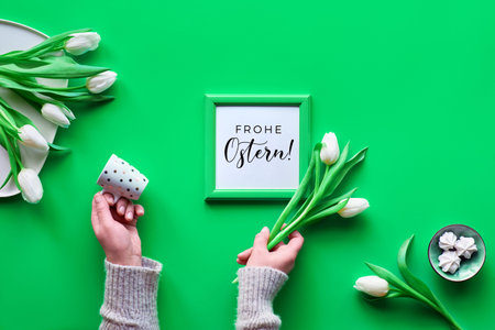 Flat lay, top view. Hands with coffee cup and white spingtime tulips, bunch of flowers on plate and...
