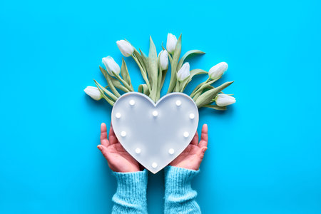 Geometric panoramic flat lay with hand showing plastic heart shaped lightboard with lights and bunch...