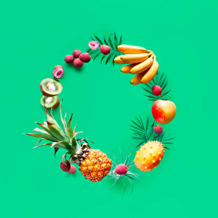 Assortment of tropical fruits flying in circle on green background. Square composition, copy-space. Pineapple, kiwano, kiwi , lichee and banana - levitation of exotic fruits.の写真素材