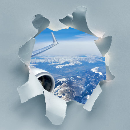 Paper hole with image of winter Alps under snow, aerial view from airplane with part of wing and a...