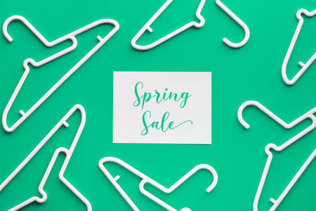 White plastic hangers, text "Spring sale" on paper. Creative top view flat lay on trendy pastel green mint background, geometric composition, creative minimalism. Flat lay, Springtime sale concept.の写真素材