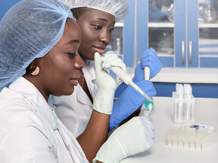 Two African scientists, technical assistants or graduates in lab coats and gloves perform PCR...