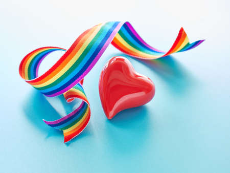 Red ceramic heart and rainbow ribbon, symbols of public support of medical teams fighting pandemics of novel coronavirus causing Covid-19 pneumonia. Curled rainbow ribbon on light mint blue backgroundの写真素材