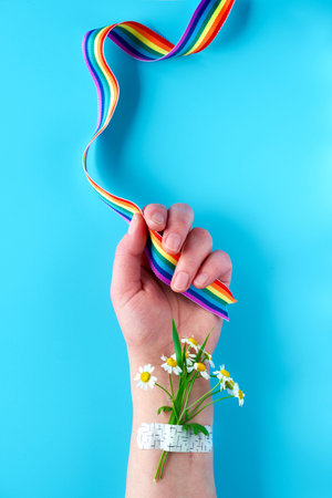 Thank you doctors and nurses! Rainbow ribbon in hand of mature woman with chamomile flowers and grass bouquet attached with medical patch. Creative flat lay, top view on blue background.の写真素材