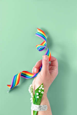 Rainbow ribbon in hand. Lily of the valley flowers, small bouquet attached to wrist with medical patch, aid band. Thank you doctors, nurses and key workers! Creative flat lay on green background.の写真素材