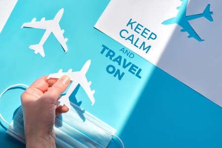Hand holding paper plane over face mask. Air travel resumes. Keep calm and travel on text. Vacations stopped and borders closed during coronavirus pandemics. Open borders, quarantine end.の写真素材