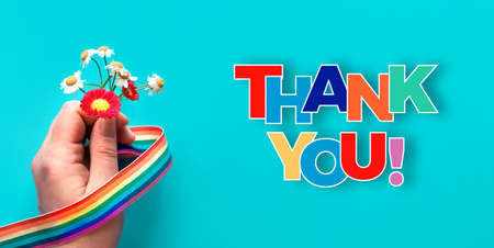Thank you doctors and nurses! Rainbow text, ribbon in hand of woman with chamomile and primrose flowers, simple bouquet. Creative flat lay, top view on turquoise blue background.の写真素材