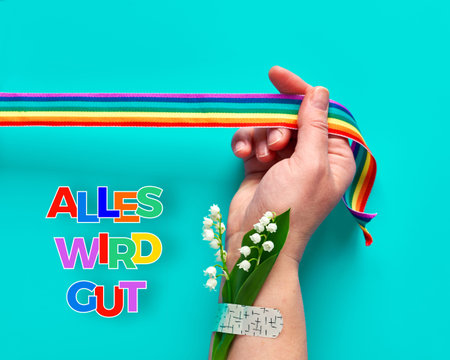 Text "Alles wird gut" in German means "Everything will be well" in English. Hand hold rainbow ribbon.の写真素材