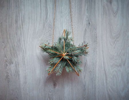Christmas wreath in a shape of golden geometric star with fir twigs hanging on rustic wooden door. Traditional Xmas ornament. Minimalist zero waste modern elegant Xmas decor.の写真素材
