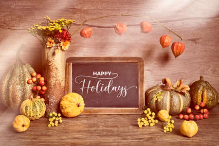 Autumn rustic decorations, text "Hello Autumn" on a black board. Natural Fall Thanksgiving, harvest concept. Autumn leaves, decorative wreath, berry, pumpkins. Eco friendly zero waste decor.の写真素材