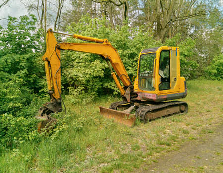 shovel excavator standing in a serene countryside at an forest pathway, green scrubland in the backgroundの写真素材