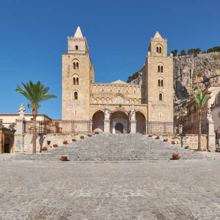 front view of   church in Cefalu sicily, decorative flowerpots line the stairs up to entrance, the mountain Rocca di Cefalu in the backgroundの写真素材