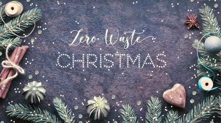 Xmas festive background with text Zero Waste Christmas. Flat lay with winter decorations, fir twigs, painted pine cones, dry lime fruit, wooden heart, cinnamon sticks and wooden cord coils.の写真素材