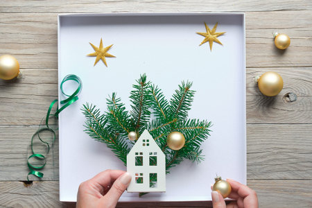 Christmas decorations, flat lay with hands making decorated box with house, fir twigs and golden...