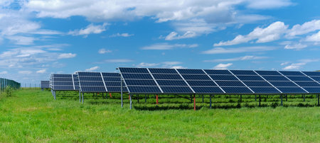 Solar power plant, blue solar panels on grass field under blue sky with clouds. Solar power...