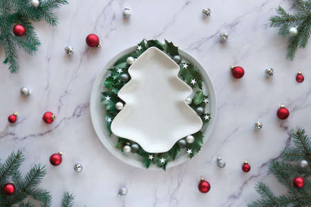 Christmas flat lay on marble table, copy-space. Xmas background in green, white and red. Natural fir twigs, holly leaves and glass trinkets.の写真素材