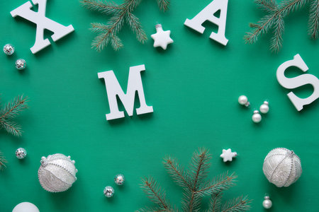 Creative Christmas flat lay with white letters Xmas on green textile. Fir twigs decorated with stars...