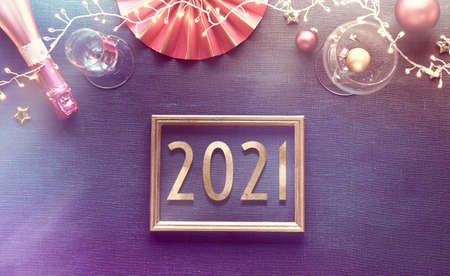 New year 2021 table setup with white plate, golden utensils, dark red napkin and gilded decorations. Flat lay, top view on dark blue linen textile background. Xmas lights garland.の写真素材