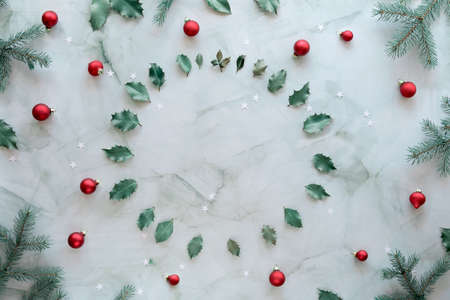 Christmas flat lay on green and red. Marble stone background, copy-space. Xmas background with natural fir twigs, holly leaves and glass trinkets.の写真素材
