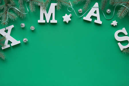 Creative Christmas flat lay with large white letters Xmas on green textile. Decorative border with copy-space. Fir twigs decorated with stars, mirror disco balls and ribbons.の写真素材