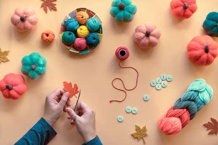 Hands with scissors cutting out Autumn leaf from felt. Hobby craft materials in Fall colors, orange, yellow, red, green. Autumn seasonal background with various felt pumpkins, wool bundle, buttons.の写真素材