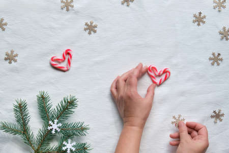Christmas flat lay with female hands holding heart from candy canes and craft paper snowflake silhouette. Zero waste eco friendly decor from natural fir Xmas tree twigs, recycled paper confetti, sweetsの写真素材