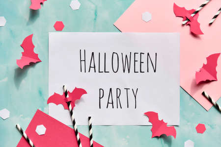 Text Halloween party on layered paper background in mint green and pastel pink. Flat lay, trendy Halloween decorations - hexagon confetti, paper drinking straws, flying bats and spiders.の写真素材