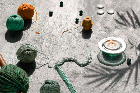 Yarn balls, crochet hook with thread, decorative felt pumpkins. Creative Autumn seasonal arrangement, craft materials for crochet on light table with tea light candle and shadows of palm leaves.の写真素材