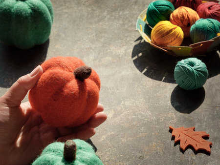 Creative arrangement of craft materials for knitting and crochet. Hand with decorative felt pumpkin,...