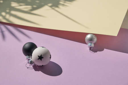 Trendy Xmas decor. Black and white Christmas toys on purple, white and yellow paper. Geometric arrangement, shadows from palm leaves.の写真素材