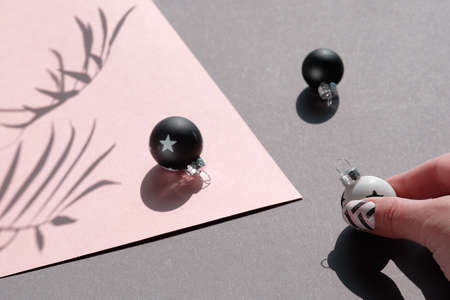 Close-up on black and white Christmas baubles on pink and grey layered paper. Geometric arrangement with shadows from the paper, trinkets and palm leaves.の写真素材