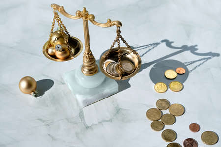 Cost of Christmas holidays concept. Weight scales, vintage balance with stack of coins and Xmas golden trinkets.の写真素材