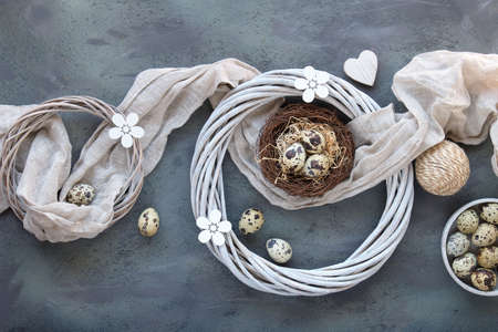 Easter flat lay with quail eggs in bird nest with linen textile. Wooden flowers and rattan wreath, Spring decor..の写真素材