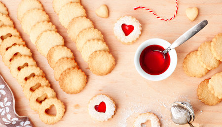 Top panoramic view of Christmas Linzer cookies filled with red jam on wooden board.