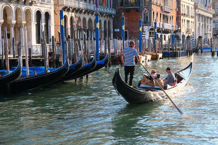 Venice, Italy - September 18, 2020: Gondolier takes tourists on his gondola on Grand Canal by gondolas moored by a shore. Venice, Italy during coronavirus pandemics.のeditorial素材