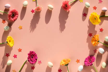 Easter creative flat lay. Frame made with marzipan Easter eggs, gerbera flowers and confetti on warm pink paper with copy-space.の写真素材