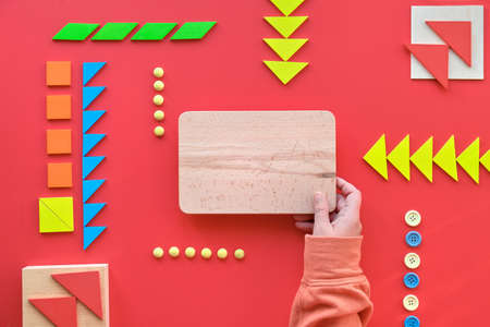 Creative design for Autism World Day on April 2. Hand hold wooden board with text space. Tangram elements, buttons arranged in order on red background.の写真素材