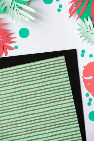 Trendy flat lay paper art on mint green, white and black layered paper. Border from exotic palm...